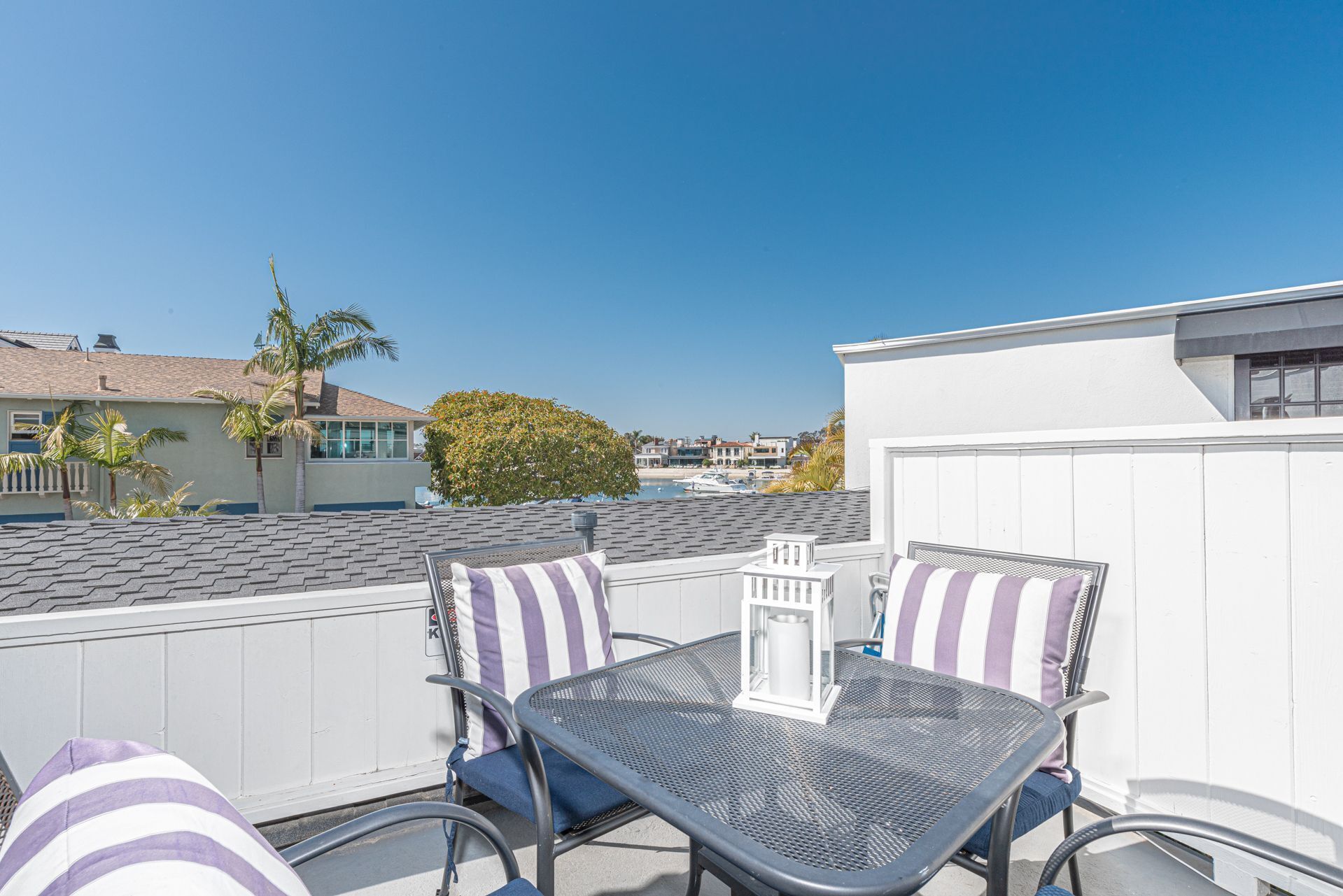 A rooftop patio with two metal tables and chairs, a white lantern, and a view of a marina with boats.