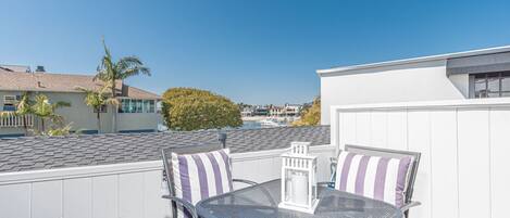 A rooftop patio with two metal tables and chairs, a white lantern, and a view of a marina with boats.