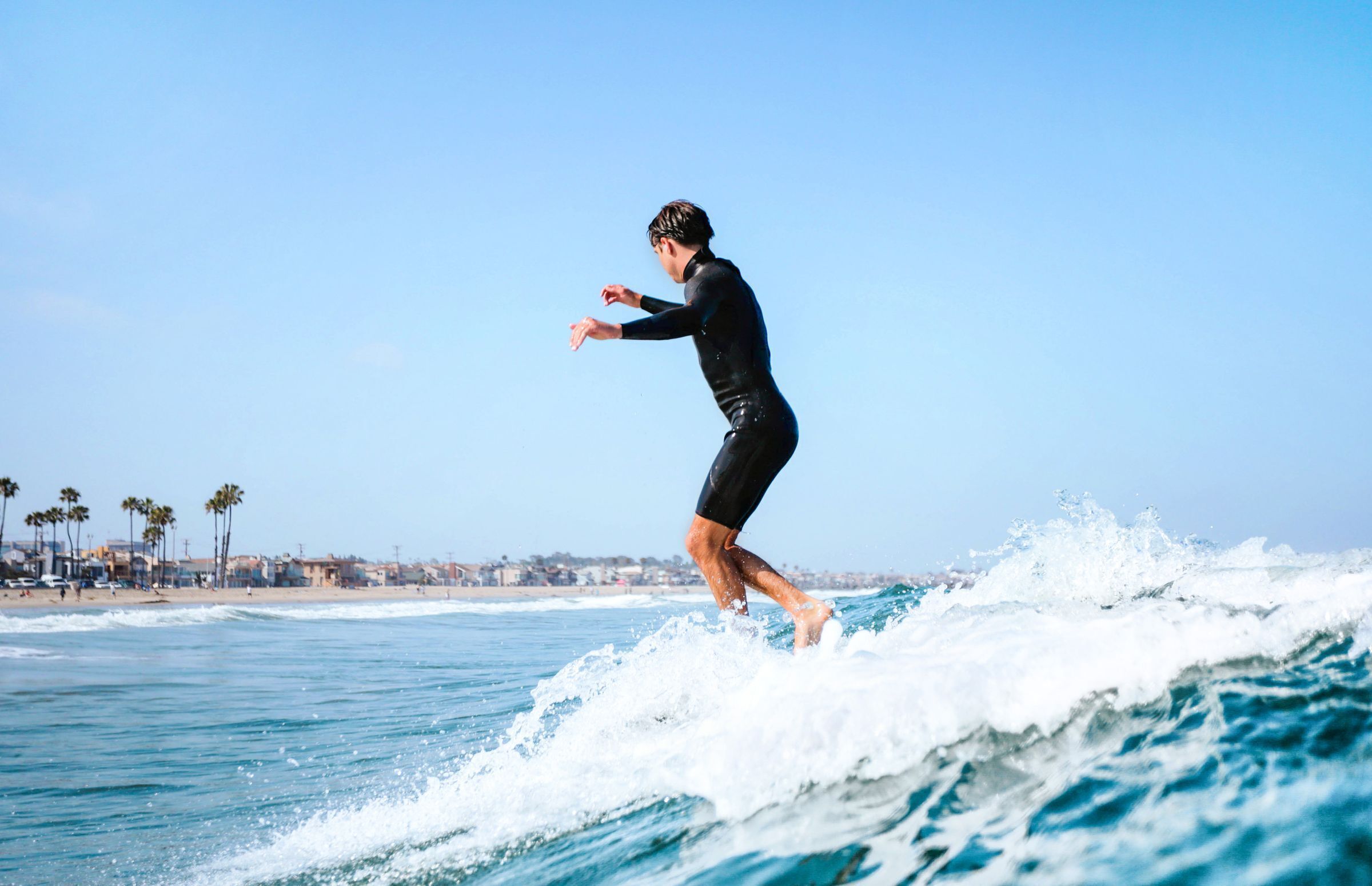 A person surfing on a wave with a clear sky and a beach in the background.