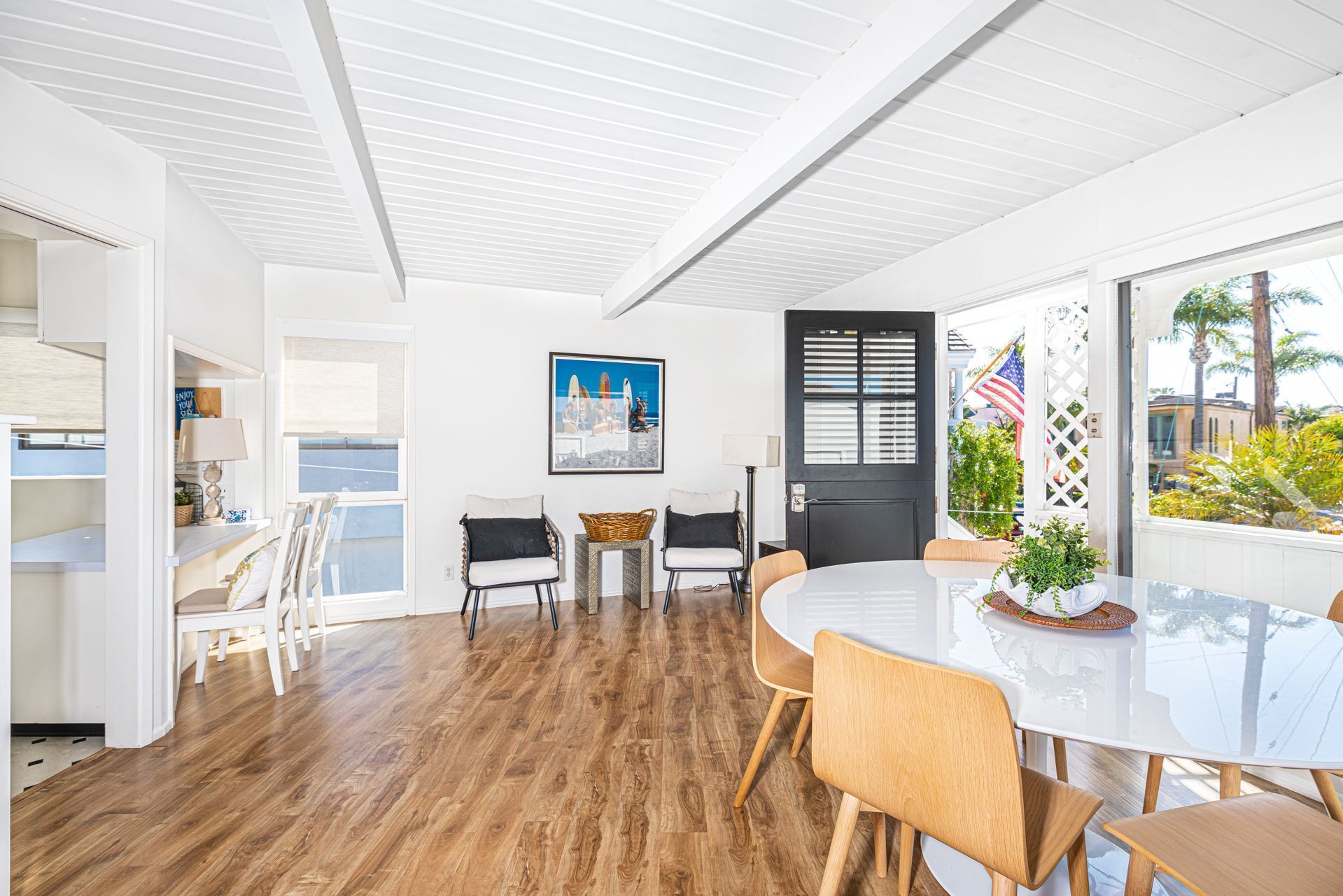 A modern dining area with a white table and chairs, a black door, and a view of the outdoors.