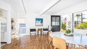 Een moderne eetruimte met een witte tafel en stoelen, een zwarte deur en uitzicht op de omgeving.