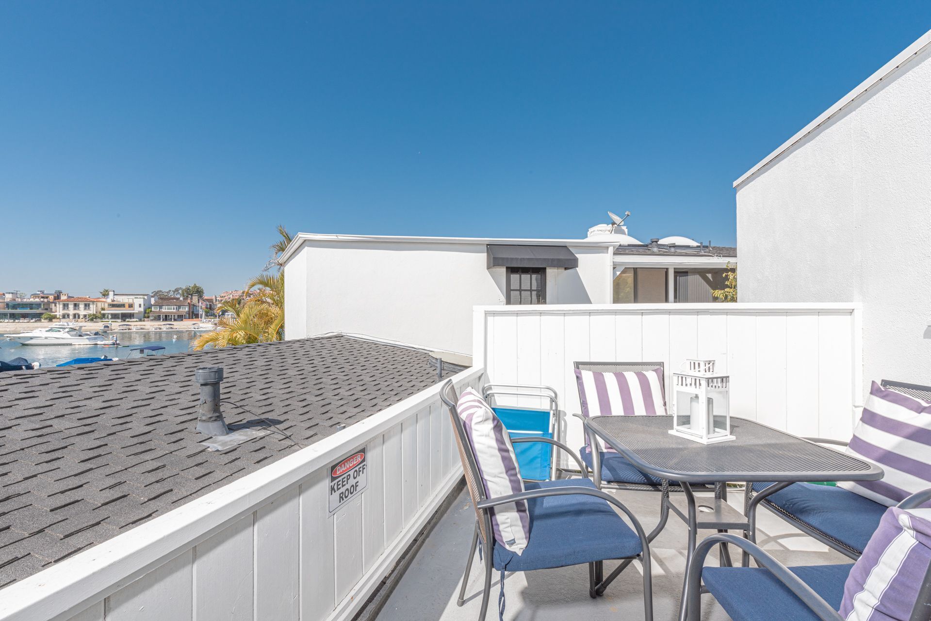 A rooftop terrace with a table and chairs, a warning sign, and a view of the marina.