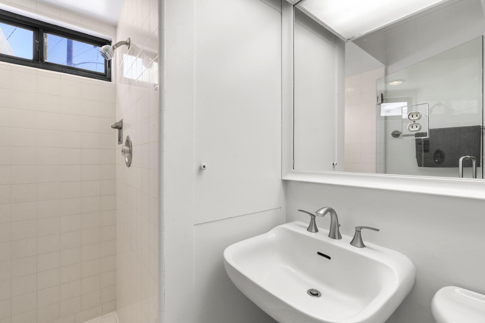 A modern bathroom with a white sink, a mirror, and a shower.