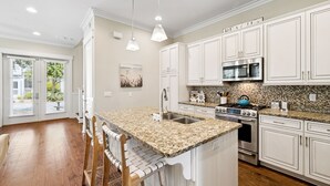Cocina moderna con armarios blancos, encimeras de granito y electrodomésticos de acero inoxidable.