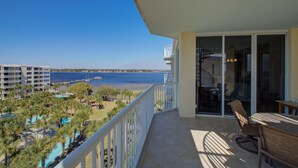 A balcony with a view of the sea, a pool area, and a dining area with outdoor furniture.