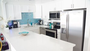 Una cocina moderna con armarios blancos, un refrigerador de acero inoxidable, un microondas y una cafetera.