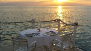 Mesa para dos en una terraza de madera con vista al océano al atardecer.