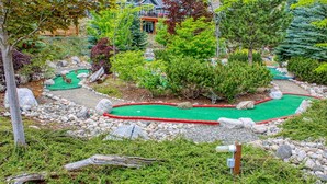 Un parcours de minigolf avec une zone d’entraînement au putting verdoyante, entourée de rochers et d’arbres.