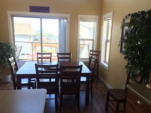 Enjoy meals in this dining area with a wooden table and six chairs, surrounded by large windows and a potted plant.