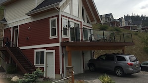 Une maison à deux étages avec une façade rouge, un balcon doté d’une balustrade noire et un garage dans lequel est garé un VUS argenté.