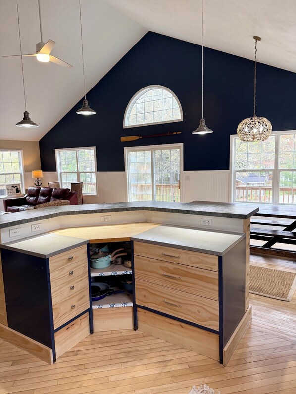 Una cocina con una isla grande, luces colgantes y vistas al exterior a través de ventanas.