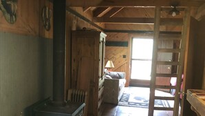 Un interior rústico de madera con chimenea, una cama y una escalera que lleva a un entrepiso.