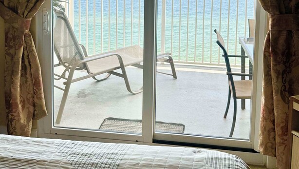 Een kamer met een bed, een balkon en uitzicht op zee, plus een stoel.