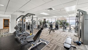 Een fitnessruimte met diverse trainingsapparaten, grote ramen en uitzicht op de oceaan.