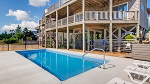A multi-story wooden building with a swimming pool, outdoor seating, and a fenced area.