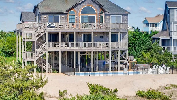 A multi-story house with a balcony, a pool, and a beach view.
