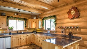 Una cocina tipo cabaña de madera con una isla central, armarios de madera y suelo de baldosas de piedra.