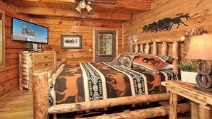 Ein Schlafzimmer im Blockhausstil mit einem Bett, einem Holz-Kopfteil, einem Deckenventilator, einem Fernseher und einer Tür mit Fenster.