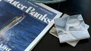 A glass bowl filled with various seashells on a table next to a magazine titled "Outer Banks Magazine 2021".