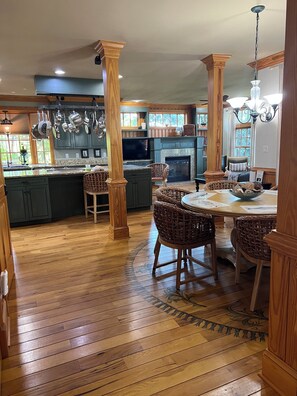 A spacious kitchen with wooden flooring, a dining area with wicker chairs, and a fireplace. - Tranquil Coastal Waterfront- Saltwater Pool/125' Private Dock/Outstanding Sunset (Kitty Hawk)