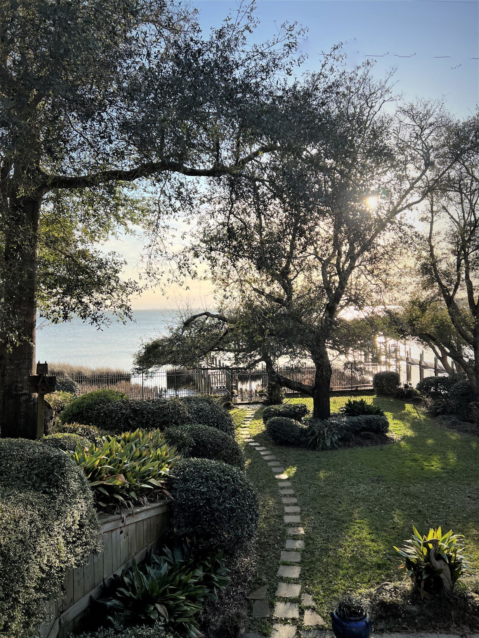 A garden with a stone pathway leading to a wooden fence overlooking a body of water.