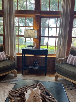 A room with a large window, a lamp, a table with a decorative item, and two chairs.