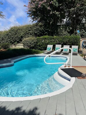 A swimming pool with a wooden deck, lounge chairs, and a wooden fence.