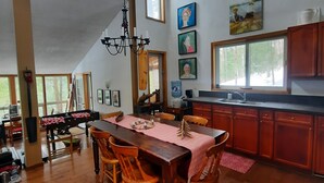 Een ruime keuken met houten kastjes, een eethoek met een grote tafel, en een vide met een schuine kap.