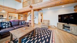 A spacious living area with a wooden ceiling, a leather sofa, a television, and a dining table.