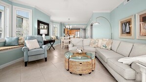 A living room with a sofa, armchair, and coffee table, a dining area with a table and chairs, and a kitchen in the background. - Beautiful Condo, Close to the Beach and Plenty of Room for Your Family! (Ocean City)