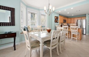 A dining area with a glass-top table, white chairs, and a chandelier. - Beautiful Condo, Close to the Beach and Plenty of Room for Your Family! (Ocean City)
