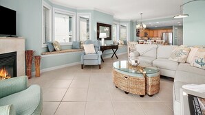 A living room with a fireplace, seating area, and a kitchen in the background. - Beautiful Condo, Close to the Beach and Plenty of Room for Your Family! (Ocean City)