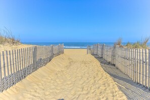 Ein Sandweg am Strand führt zum Meer, gesäumt von Holzzaunen.