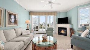 A living room with a sofa, armchair, glass coffee table, fireplace, television, and artwork on the wall. - Beautiful Condo, Close to the Beach and Plenty of Room for Your Family! (Ocean City)