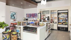 A clean, well-organized shop with a variety of snacks and beverages, a coffee machine, and a sign indicating the shop's name. - Hilton Garden Inn Denver/Thornton (Thornton)