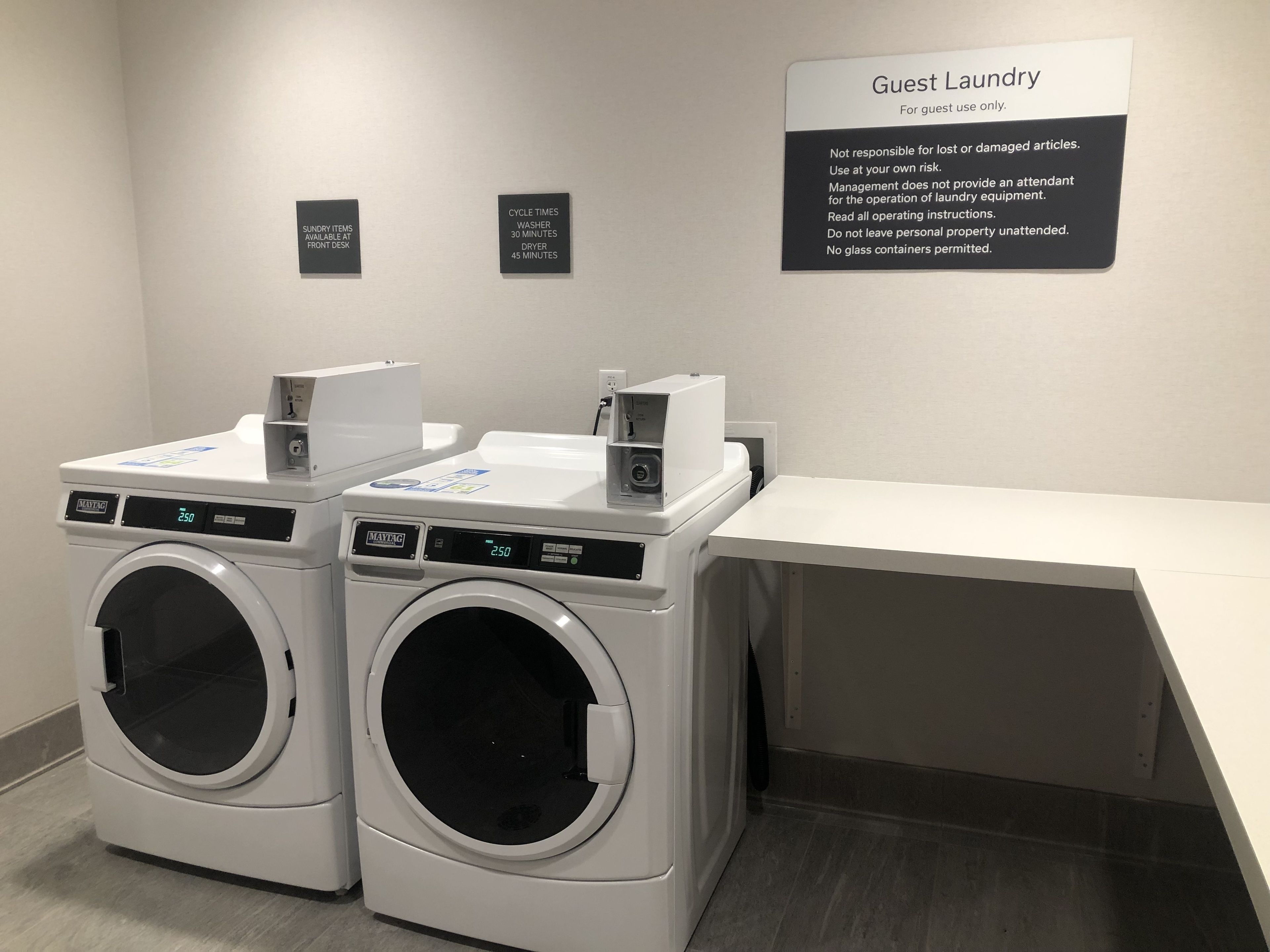 Uma área de lavandaria para hóspedes, com duas máquinas de lavar Maytag, um local para secar roupas e um aviso com instruções de uso.
