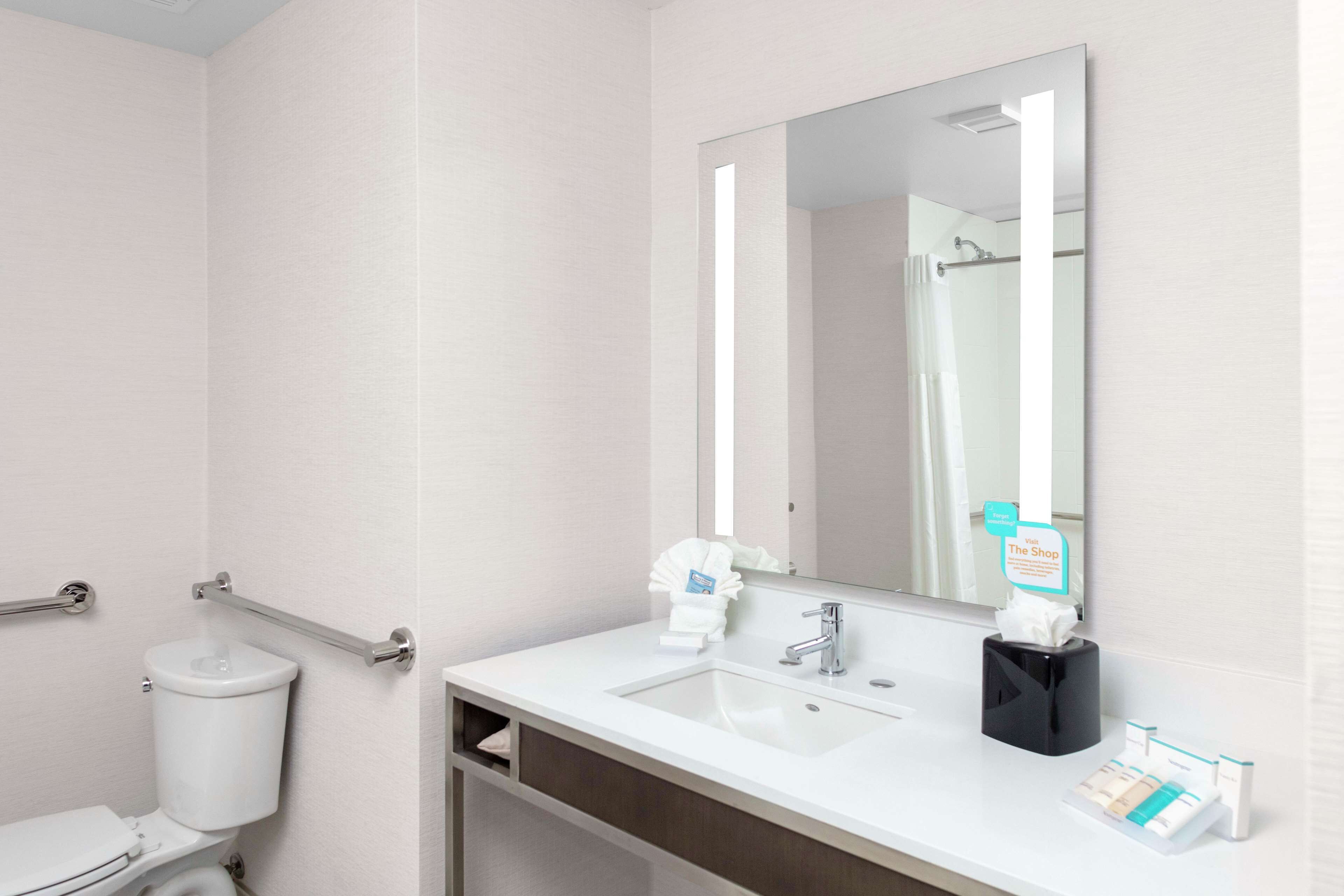Une salle de bain moderne avec un lavabo blanc, un miroir, des toilettes et une barre d’appui.