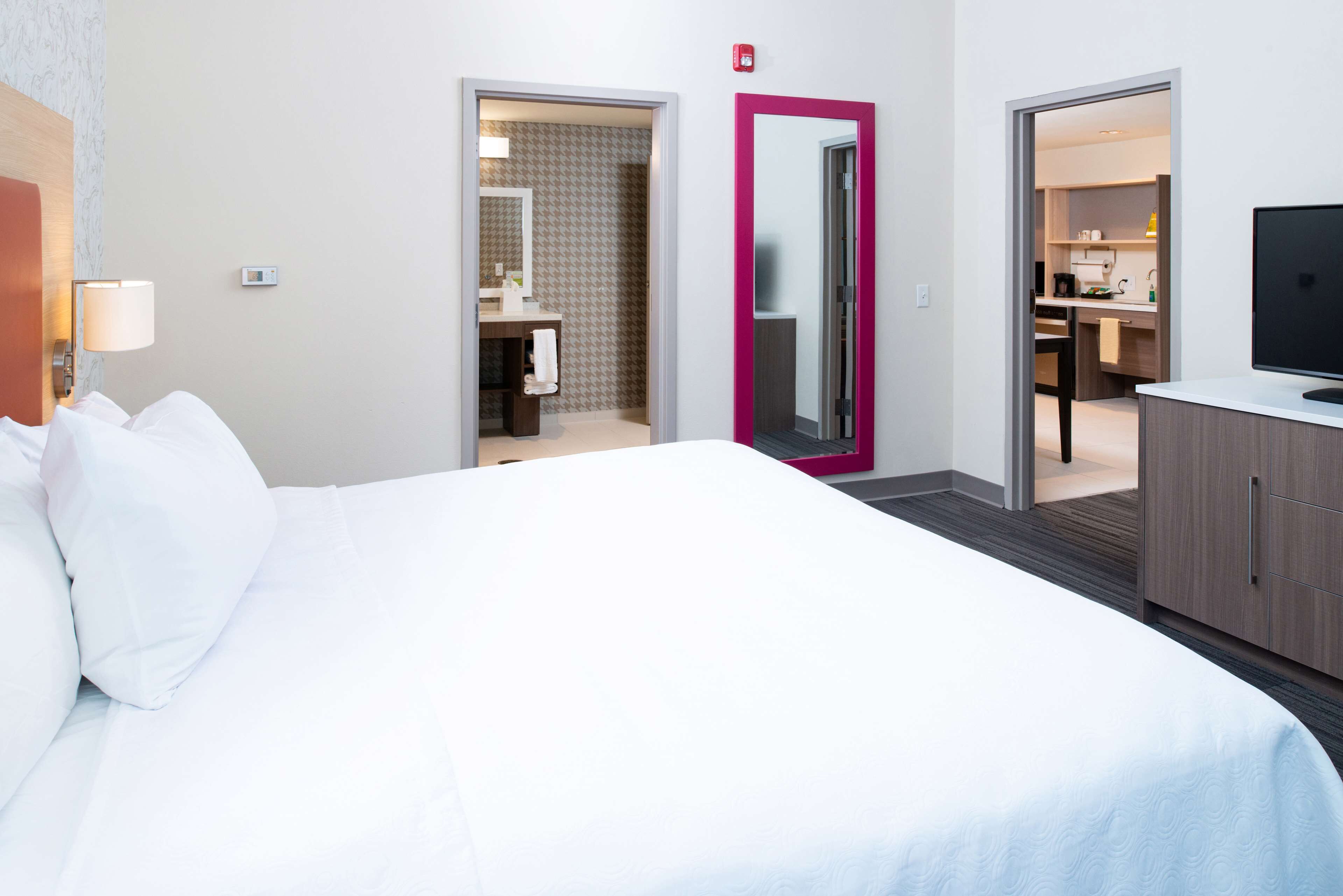 A hotel room with a large bed, a bathroom with a mirror, and a kitchenette.