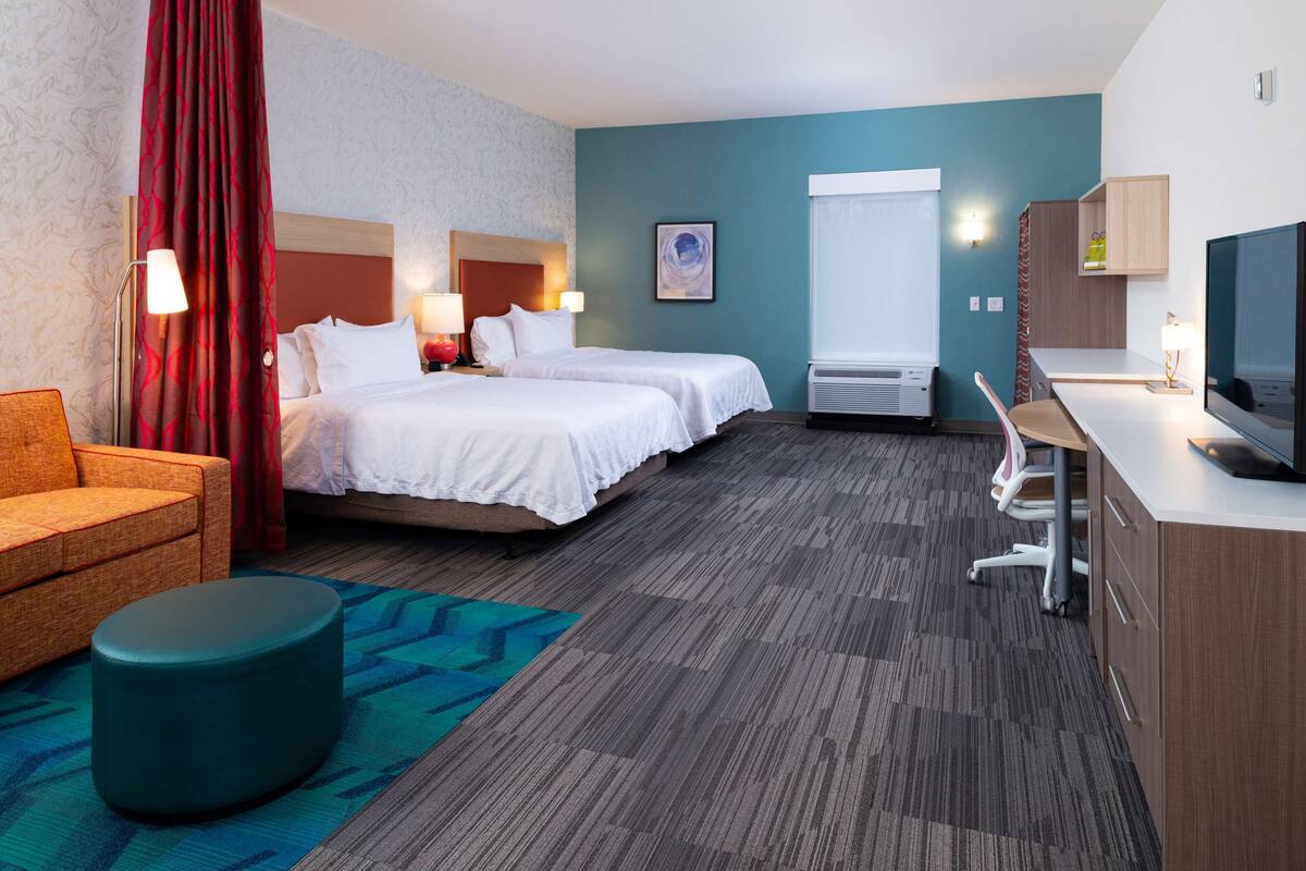 A hotel room with two beds, a desk, a television, and a seating area.
