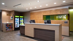 Zona de recepción de hotel con mostrador, un refrigerador y una máquina expendedora.