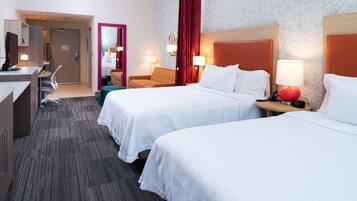 Quarto de hotel com duas camas, uma escrivaninha, uma cadeira e uma pequena mesa com abajur.