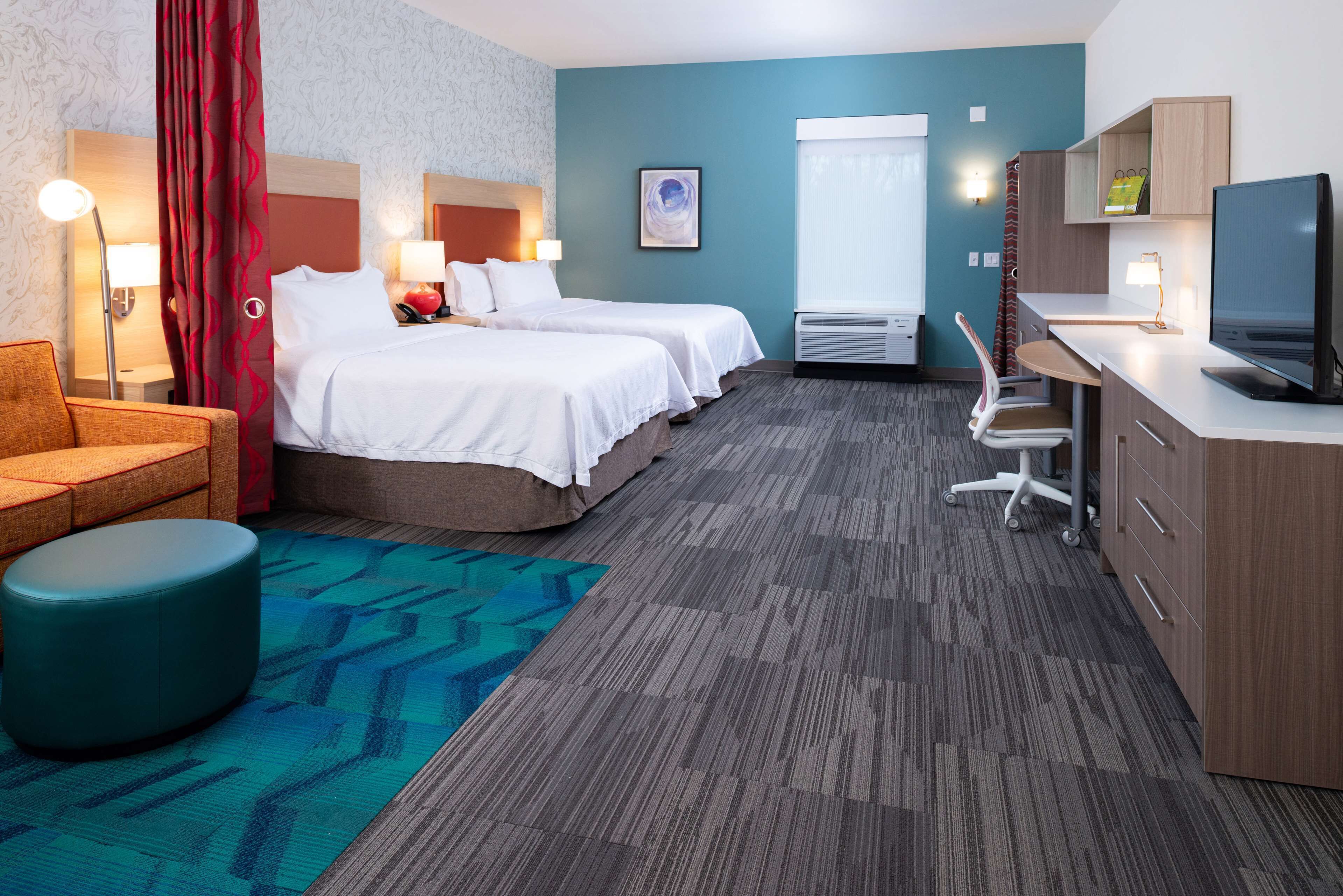 A hotel room with two beds, a desk with a TV, a chair, a sofa, and a large window.