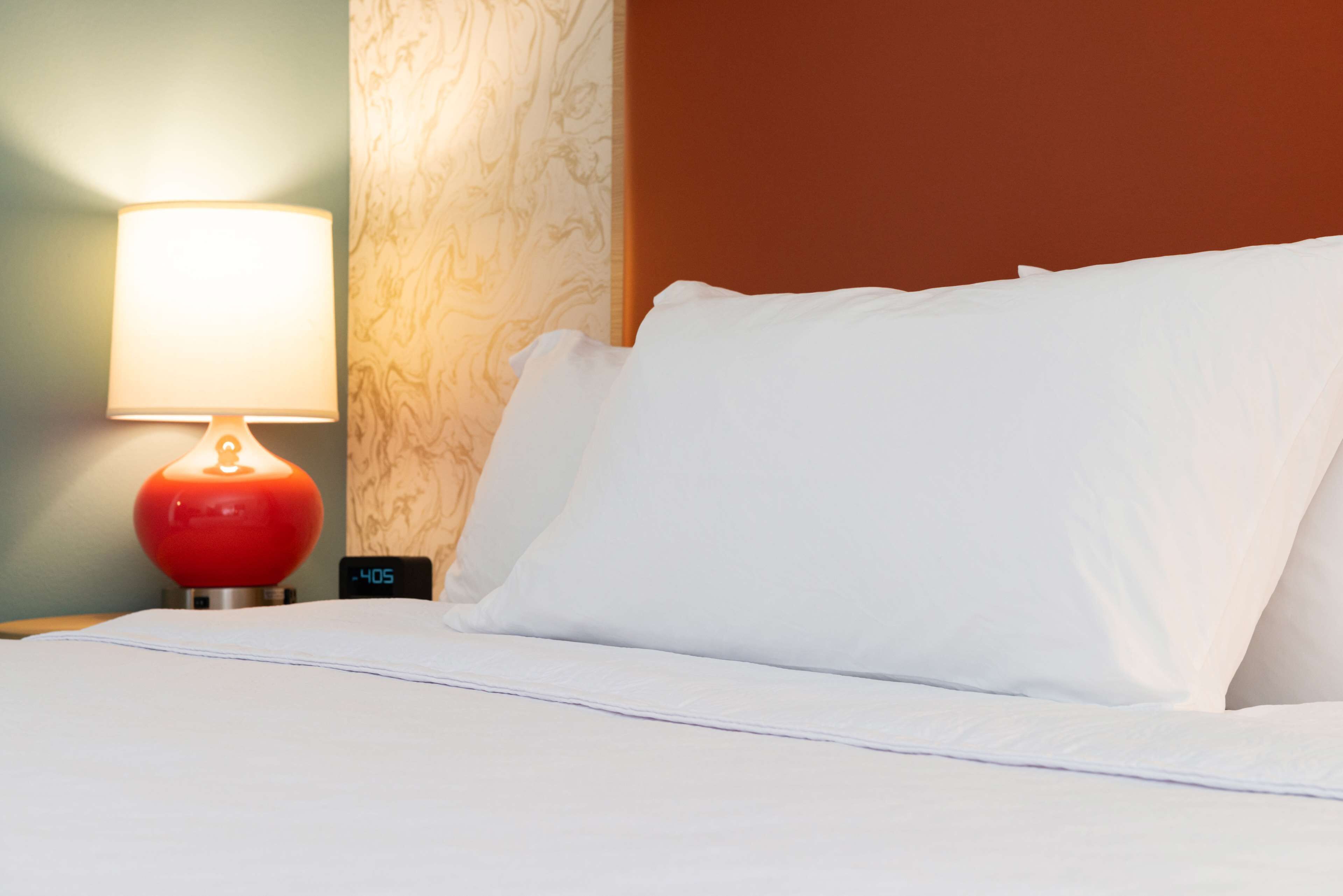 Habitación de hotel con cama, lámpara roja y un reloj marcando las cuatro y cinco.