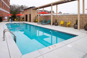 A swimming pool with lounge chairs and umbrellas, surrounded by a brick wall and a covered patio area.