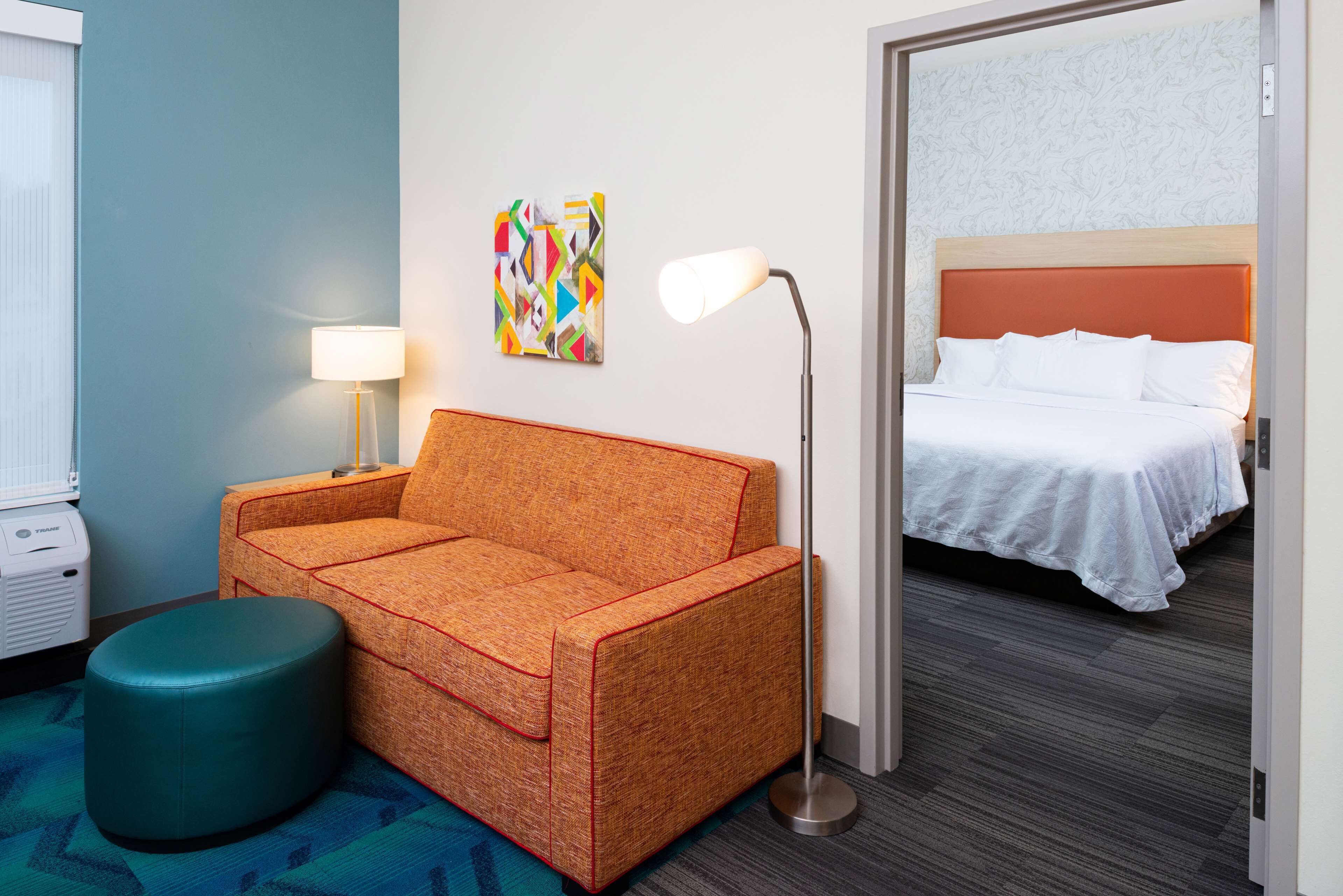 Ein Hotelzimmer mit einer Couch, einer Stehlampe, einem Bett und einem farbenfrohen Kunstwerk an der Wand.