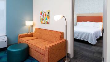 Ein Hotelzimmer mit einer Couch, einer Stehlampe, einem Bett und einem farbenfrohen Kunstwerk an der Wand.