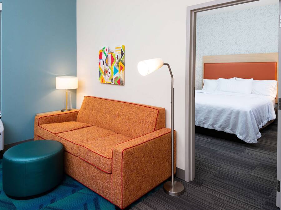 Ein Hotelzimmer mit einer Couch, einer Stehlampe, einem Bett und einem farbenfrohen Kunstwerk an der Wand.