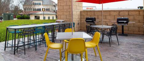 An outdoor patio with tables and chairs, red umbrellas, and a grill.