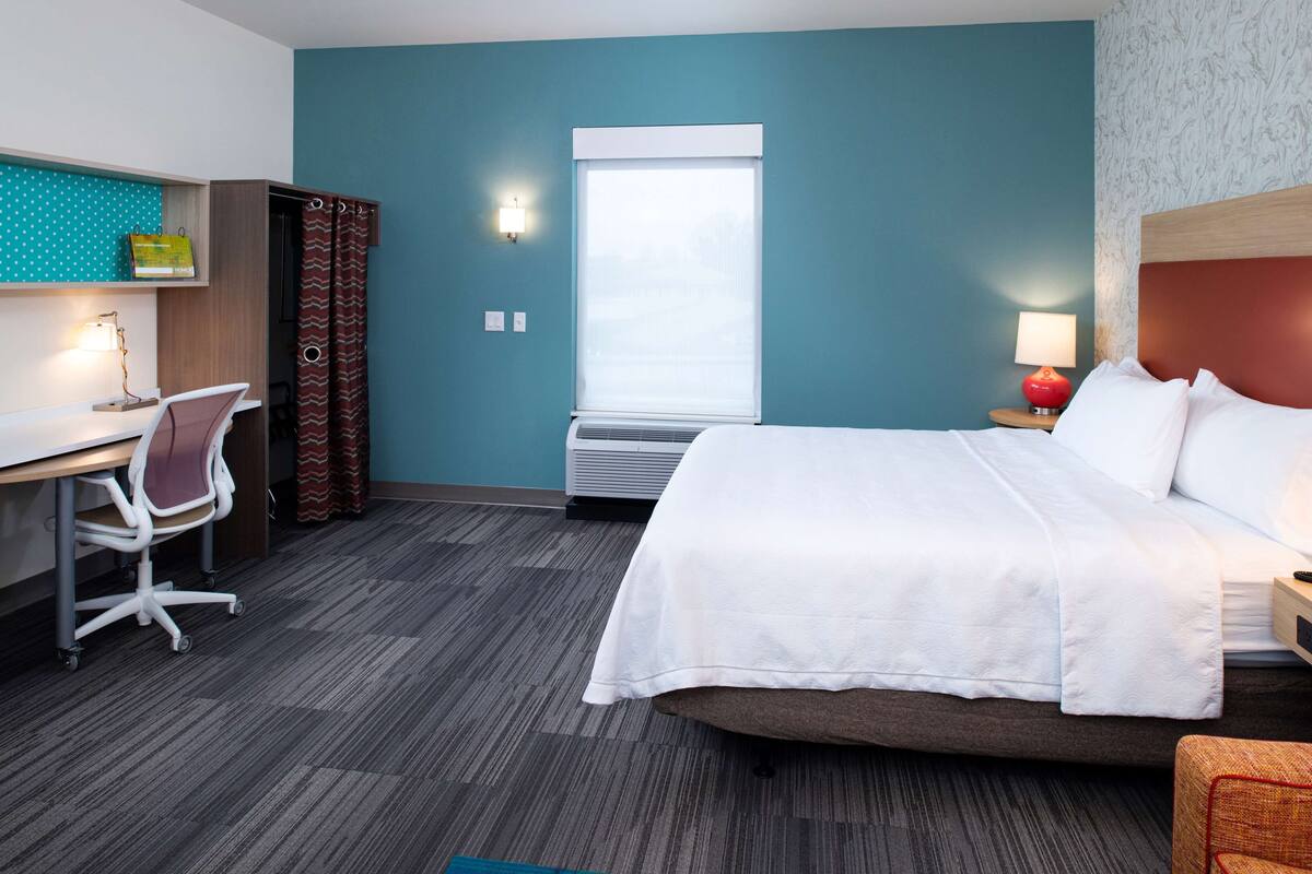 A hotel room with a bed, desk, chair, and a window with curtains.