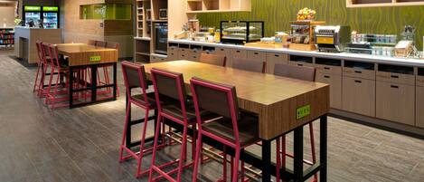 Un área de desayuno moderna con una mesa de madera y sillas rojas, una barra con alimentos y un letrero que dice 'Good Morning'.